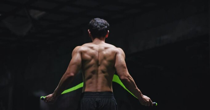 Young handsome Caucasian man boxer jump rope exercises in abandoned building hall gym under smoke light. Skipping man working out in cross training space in slow motion. Silhouette on dark background