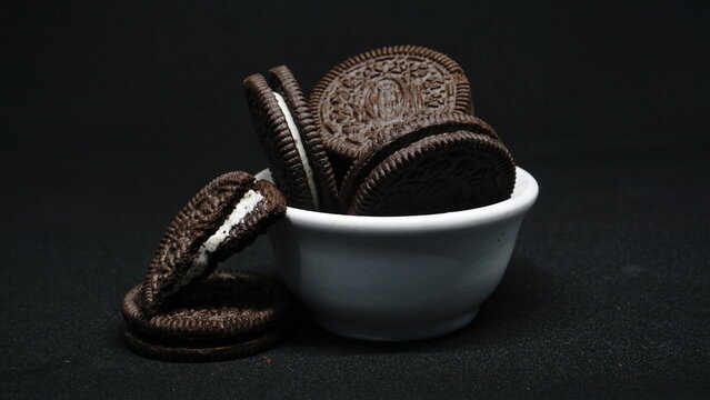 A bowl of Cookies isolated on black background. Chocolate cookies with white cream filling on white bowl