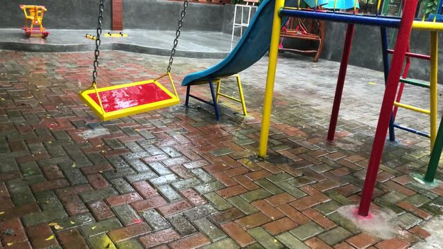 Empty swing swaying playground during rain.