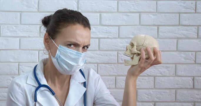 Doctor head skeleton. A doctor in mask hold a skull in hand. A concept of medical error and health problems during coronavirus pandemic.