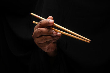 Asian male dark skinned single hand fist finger on black background holding chopsticks feed eat