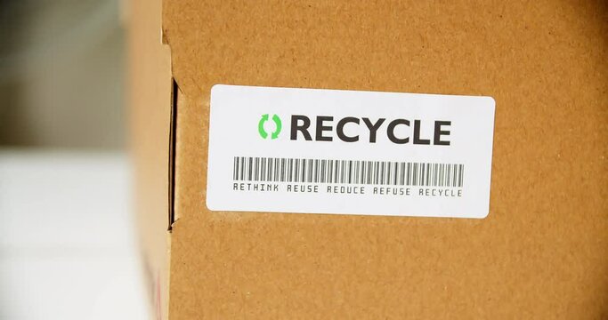 Hands applying RECYCLE Sticker label on a cardboard box with barcode rethink reuse reduce refuse.