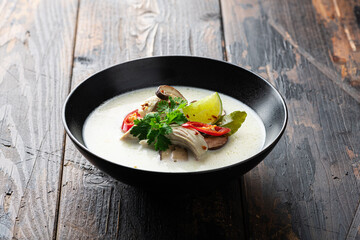 Tom Kha Gai, Thai Galangal coconut soup in a black bowl on a wooden background, selective focus