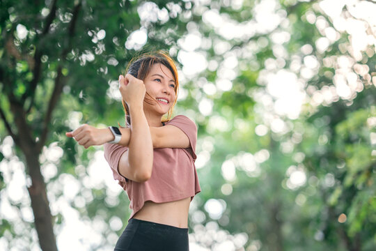 Fitness woman doing stretch exercise stretching her arms, female stretching for warming up before running or working out in the park outdoor.