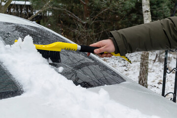 Man brushing snow and ice from windscreen of car with brush. Person cleaning fresh snow after snowstorm from car in the winter. Snow layer on windscreen, window. vehicle in extreme weather conditions