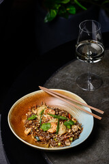 Thai buckwheat noodles with shrimp in a plate on a gray table with a glass of wine