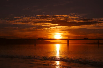 Obraz premium Beautiful red orange sunset over the surface of the river and the bridge. Summer nature landscape