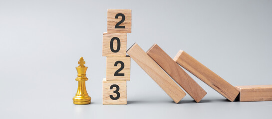 wooden Dominoes falling against 2023 stop blocks with golden Chess King figure. Business, Risk...