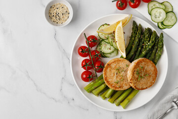 Baked cutlets with vegetables - asparagus, cucumbers and tomatoes cherry on white plate. Diet dinner idea, keto diet. Fish cutlets.