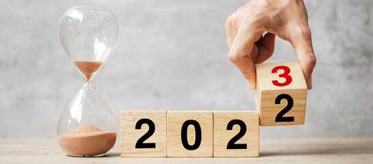 hand flipping block 2022 to 2023 text with hourglass on table. Resolution, time, plan, goal,...