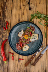 veal tartar in a blue plate on a wooden background with utensils and spices vertical photo
