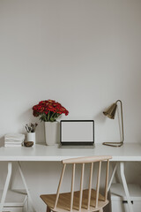 Laptop computer with blank copy space display on table with stationery, flowers bouquet, lamp. Aesthetic minimalist home office workspace. Mockup template