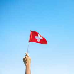 hand holding Switzerland flag on blue sky background. Switzerland National Day and happy...