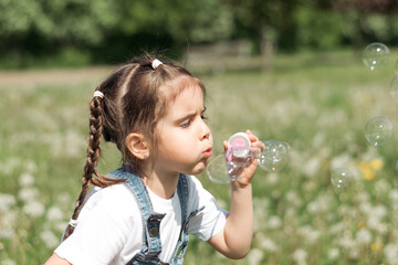 Portrait of a happy little caucasian girl blowing soap bubbles on a summer day in the park.Summer, childhood concept.