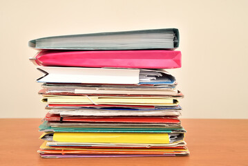 Stack of colorful document file folders on the brown wooden office desk. Close-up. 