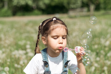 Portrait of a happy little caucasian girl blowing soap bubbles on a summer day in the park.Summer,...