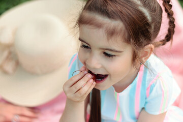 Close-up of cute little girl playing with cherry berries on a summer day in the park on a picnic.Summer, childhood concept.
