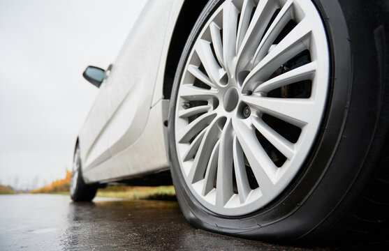 Close up view on stopped white car with punctured car tire on a road. Focus on a wheel.