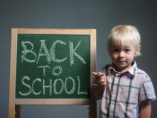 Back to school. The blonde boy write a chalk inscription on the board. Schoolboy from primary school. Happy pupil 
