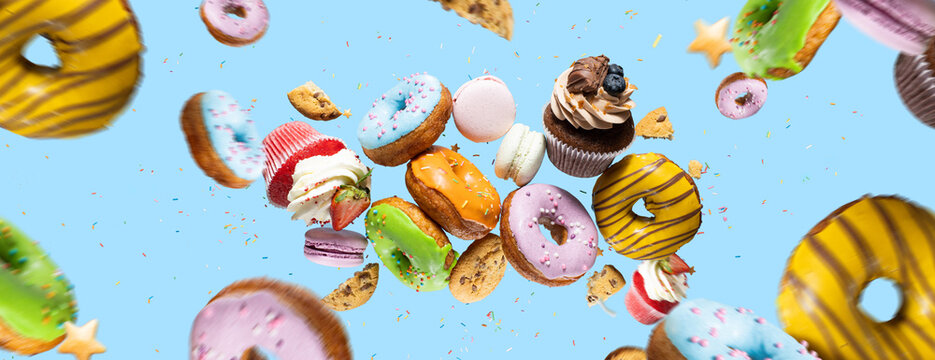 Confectionery as cakes, sweets, dougnuts collage on background. Colorful donuts, cookies, cupcakes, macaroons flying over blue background