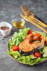 Fresh vegetable salad and baked salmon in a plate on the table. Mediterranean diet concept