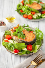 Fresh vegetable salad and baked salmon in a plate on the table. Mediterranean diet concept