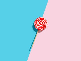 Red and white colored swirl round candy lollipop on pink and blue duotone background.