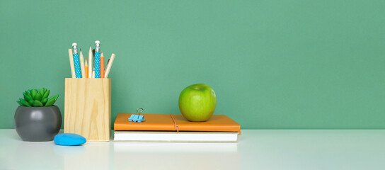 School equipment on white table, green wall background. Education backdrop. Wooden school supplies, notepad, pencils and cactus plant. Back to school. Student Desk. Stationery for study. Work at home