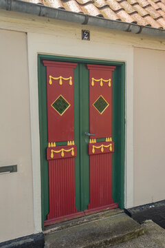 03-07-2022 Assens, Denmark. Old wooden door, painted in castle red. Green frames and panes shaped peephole