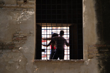 Couple are climbing on a window of an abandoned building. The couple can be seen through the bars.