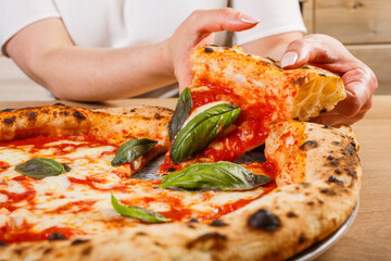 Fetta di pizza margherita napoletana con sugo di pomodoro, mozzarella basilico fresco tra le mani di una cliente - obrazy, fototapety, plakaty