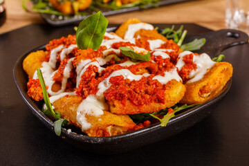 Paccheri fritti ripieni di ricotta e conditi con sugo di pomodoro, crema di formaggio e basilico fresco serviti come antipasto in una pizzeria 