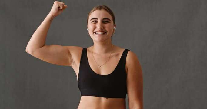 Young Caucasian woman smiling while doing arm flexing with ear pods in her ears