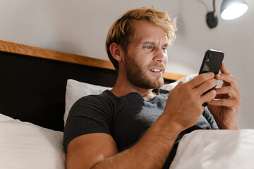 Blonde bearded man using mobile phone while lying in bed