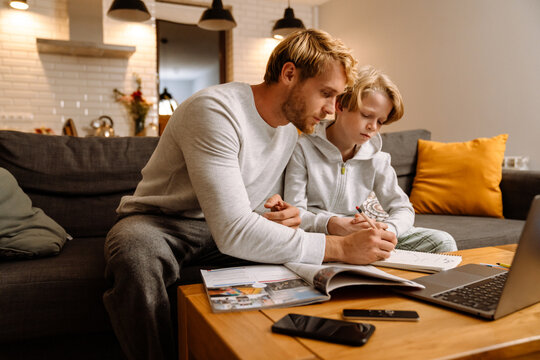 Ginger boy using laptop while doing homework with his father