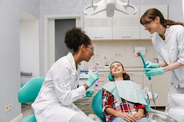 Obraz premium Two multiracial dentists talking with patient in dental clinic