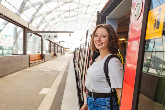 Smiling teenage girl standing at doorway of train at railroad station