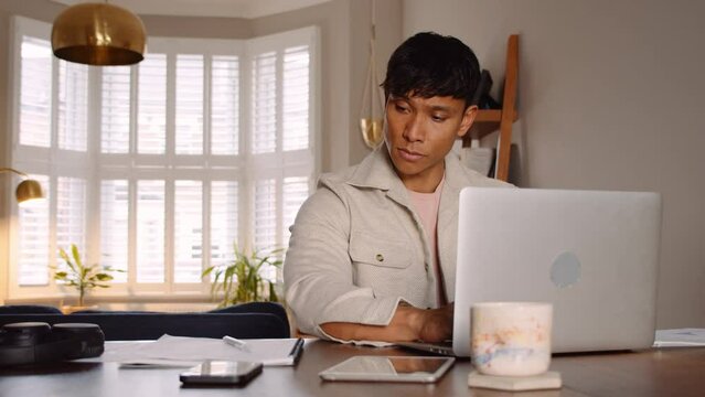 Asian man typing on laptop and taking notes