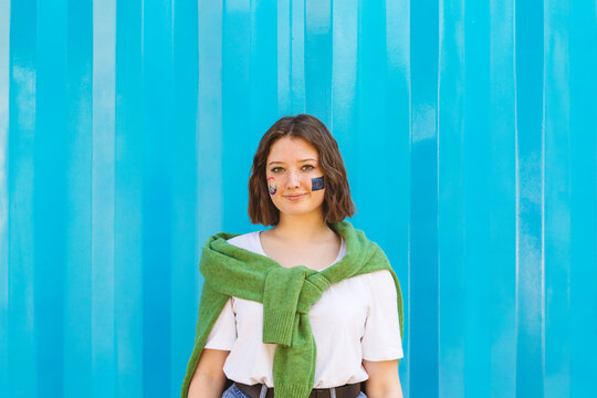 Smiling teenage girl with peace symbol and European Union paint on cheeks standing in front of blue cargo container