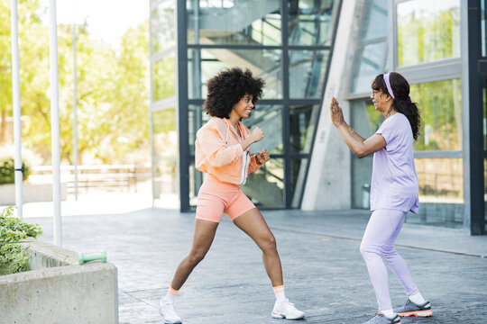 Afro woman doing boxing with mother on footpath