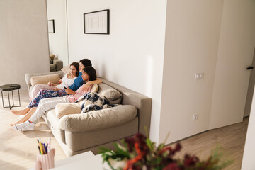 White woman and her daughters watching tv while resting on couch