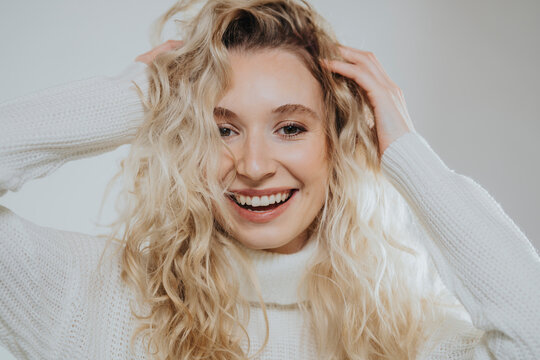 Happy blond woman with hand in hair against white background