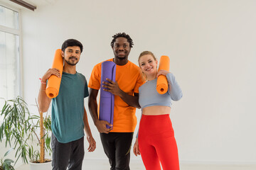 Smiling woman and men holding exercise mats in yoga studio