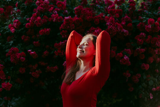 Happy woman with hands behind head enjoying sunlight in front of rose plant