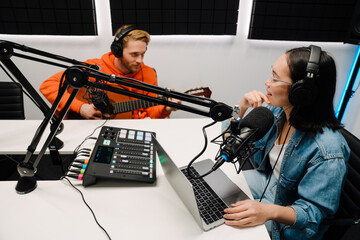 Young man playing guitar while woman recording podcast in radio studio