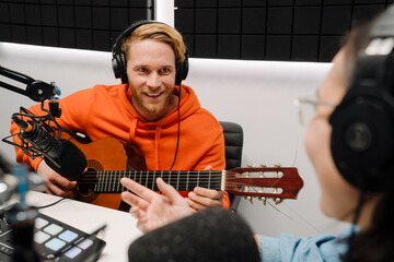 Young man playing guitar while woman recording podcast in radio studio