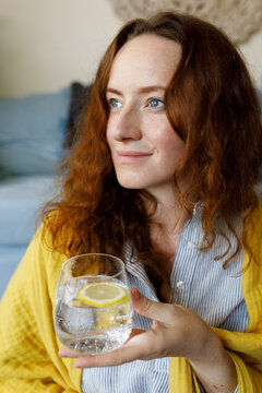 Contemplative Woman Holding Glass Of Sparkling Water With Lemon Slice