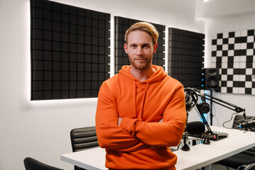 Bearded white young man standing by radio workplace in studio