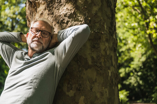 Senior man with eyes closed leaning on tree trunk