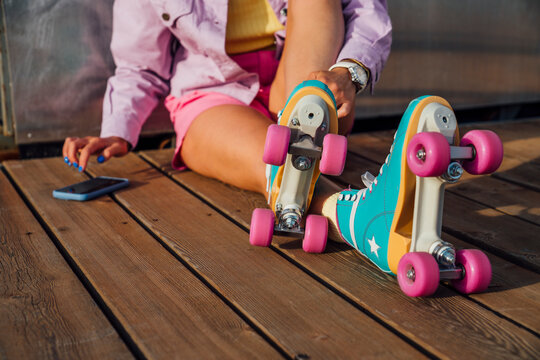Woman wearing roller skates using mobile phone sitting on floorboard
